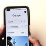 A close-up of a hand holding a smartphone with Google search displayed on the screen.