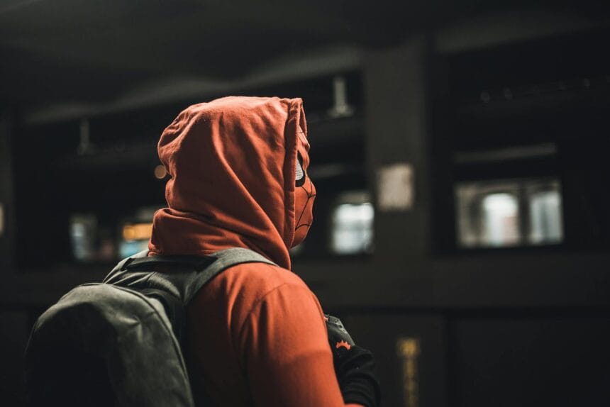 Portrait of an adult in a Spider-Man costume carrying a backpack in an urban subway station.
