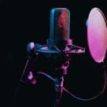 Close-up image of a condenser microphone with a pop filter in a studio setting, featuring atmospheric lighting.