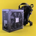 Black Chieftec power supply unit with cables against a vibrant yellow background.