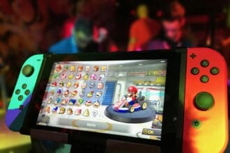 Close-up of a Nintendo Switch showing Mario Kart selection screen, gaming atmosphere in the background.