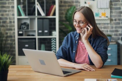 a woman talking on a cell phone while using a laptop